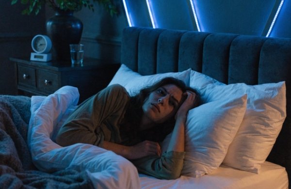 Person lying in bed at night with cool/blue LED strip lights glowing on the wall or ceiling, showing the typical unsafe nighttime setup