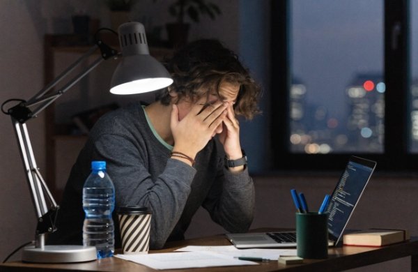 Person rubbing tired eyes while working under harsh cool blue LED light at night